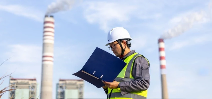 Environmental compliance engineer reviewing emissions monitoring data at an industrial facility for ISO 14001 compliance